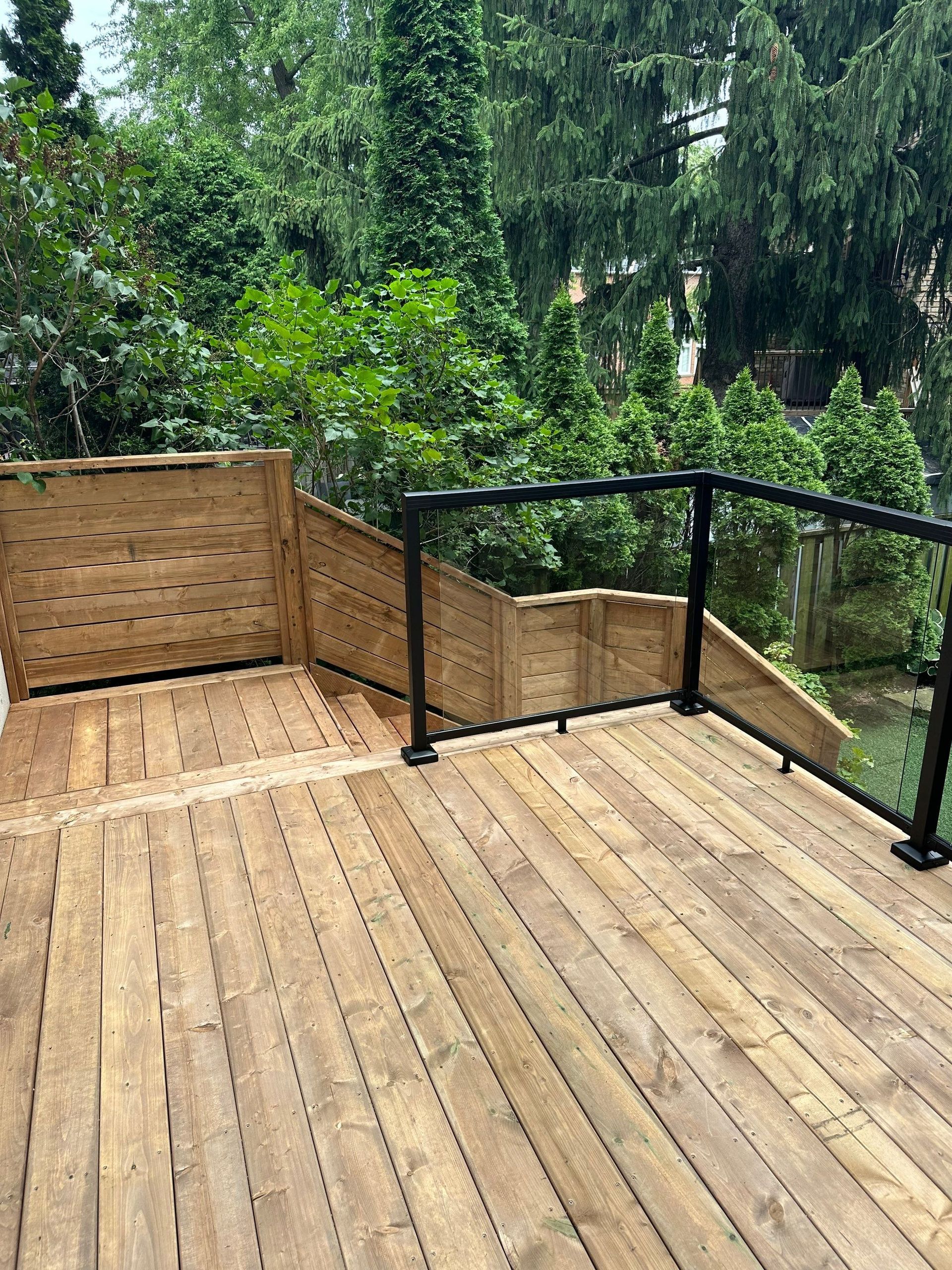A wooden deck with a glass railing and trees in the background.