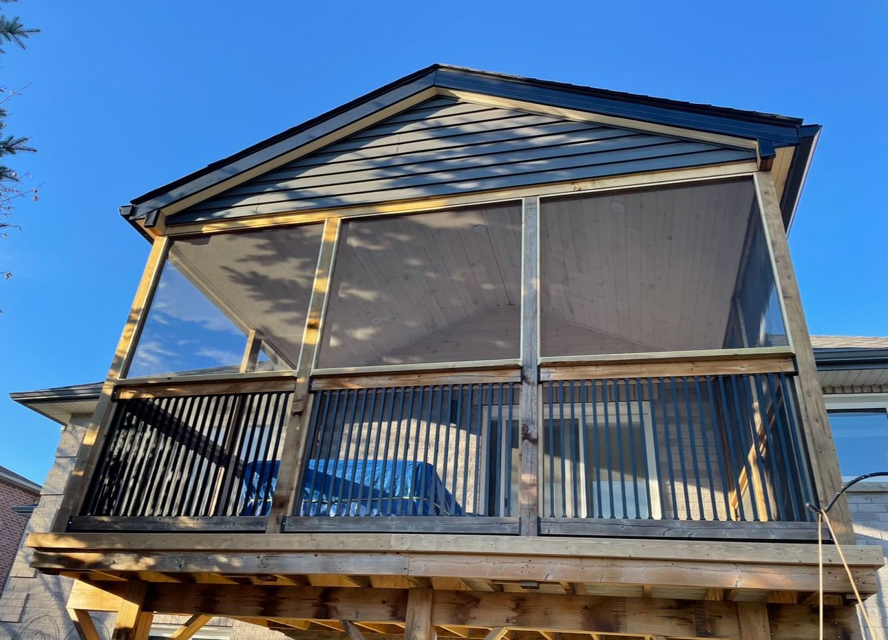 A screened in porch on top of a house with a blue sky in the background.