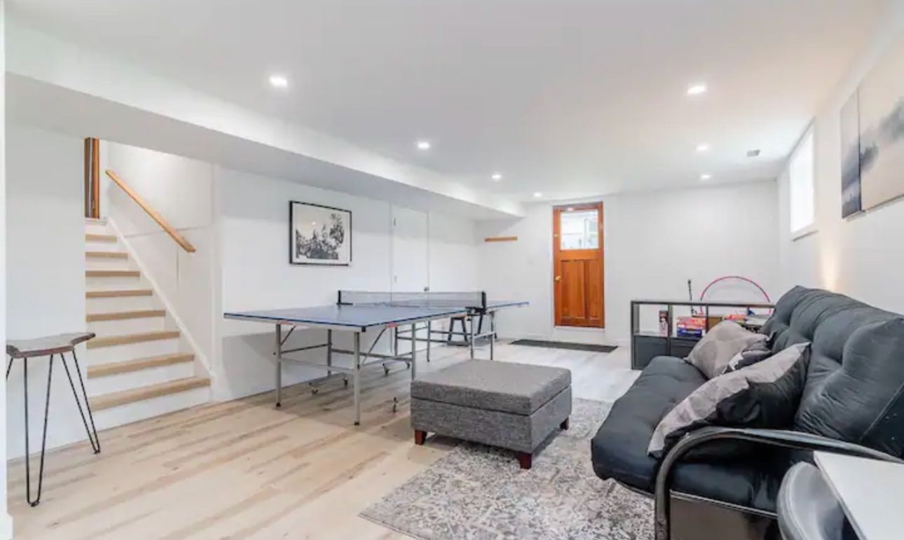A living room with a couch , ottoman , table and stairs.