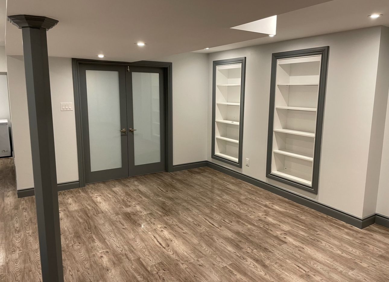 An empty basement with hardwood floors and shelves.