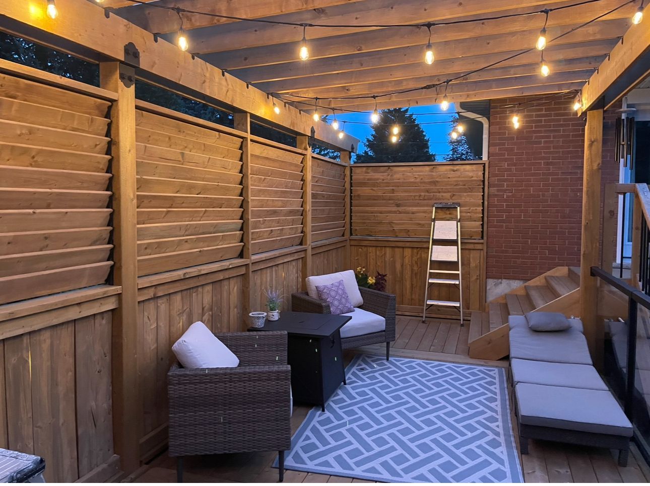 A patio with a pergola , chairs , a table and a rug.