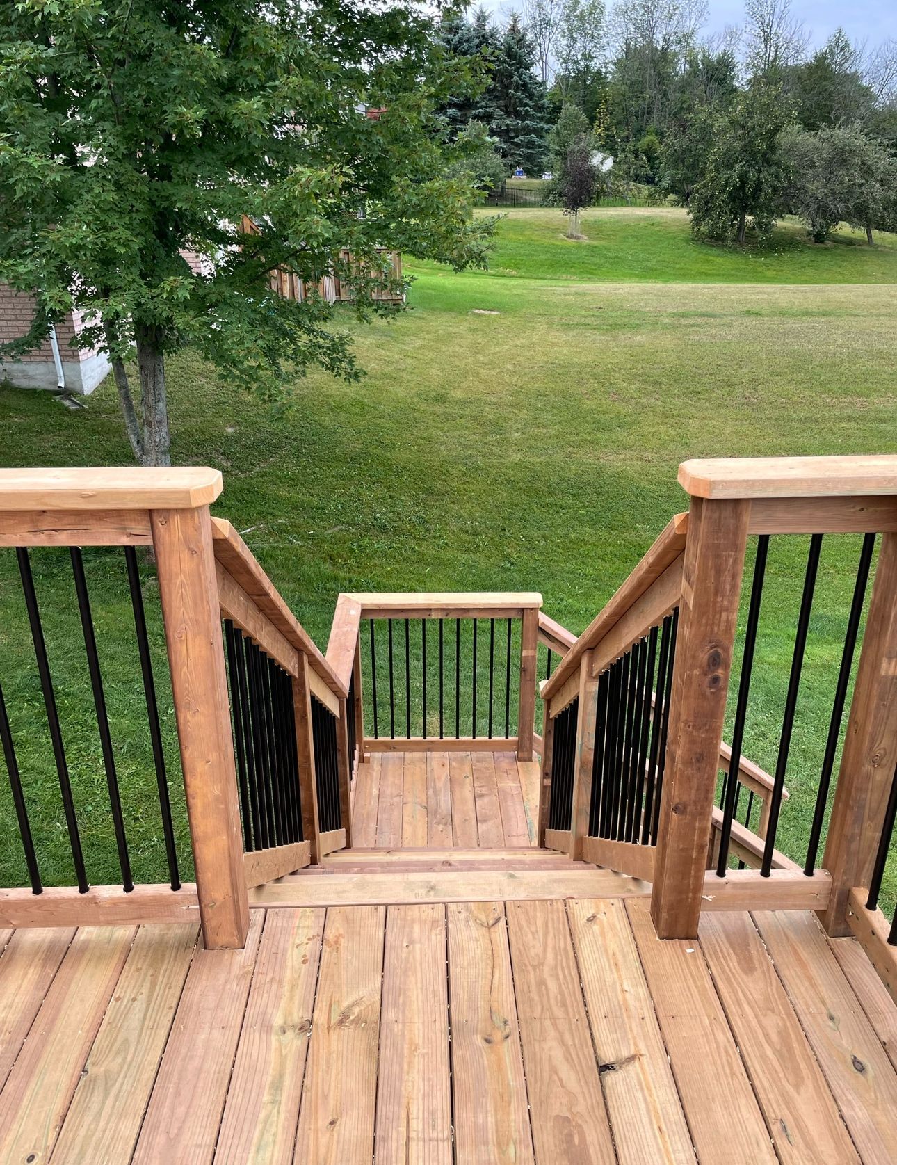 A wooden deck with stairs leading up to a grassy field.