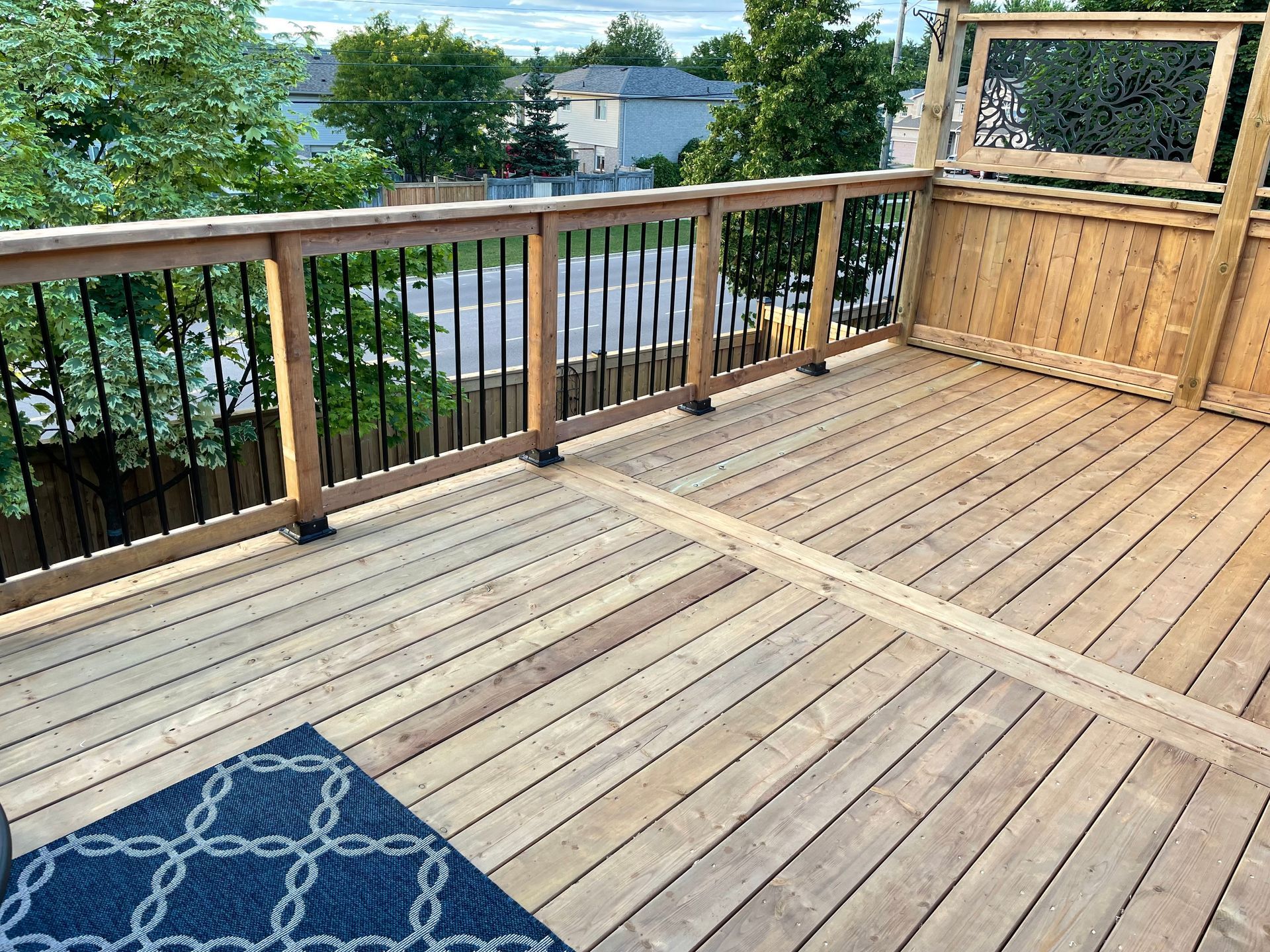 A wooden deck with a black railing and a blue rug.