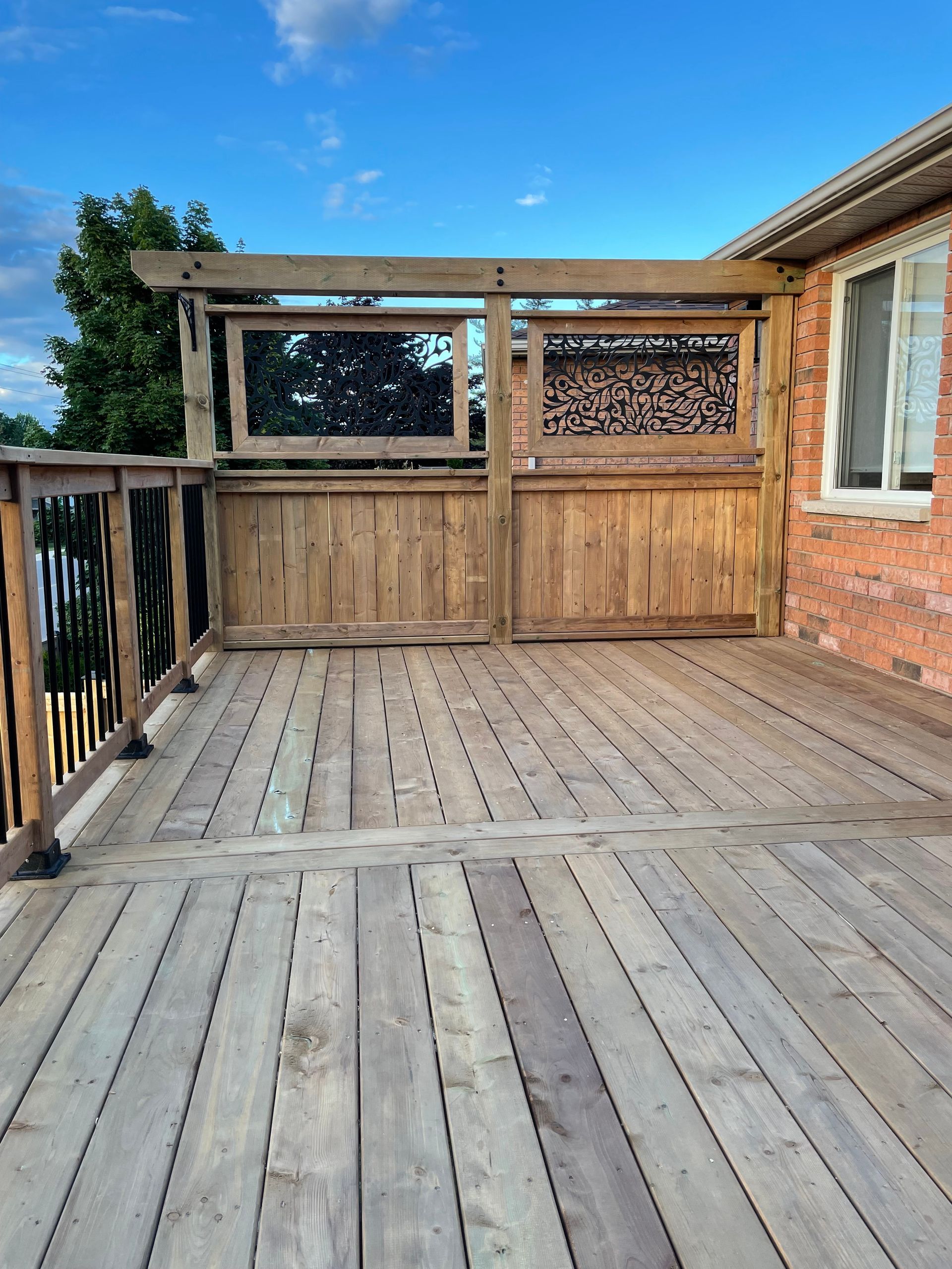 A wooden deck with a fence and a brick building in the background.