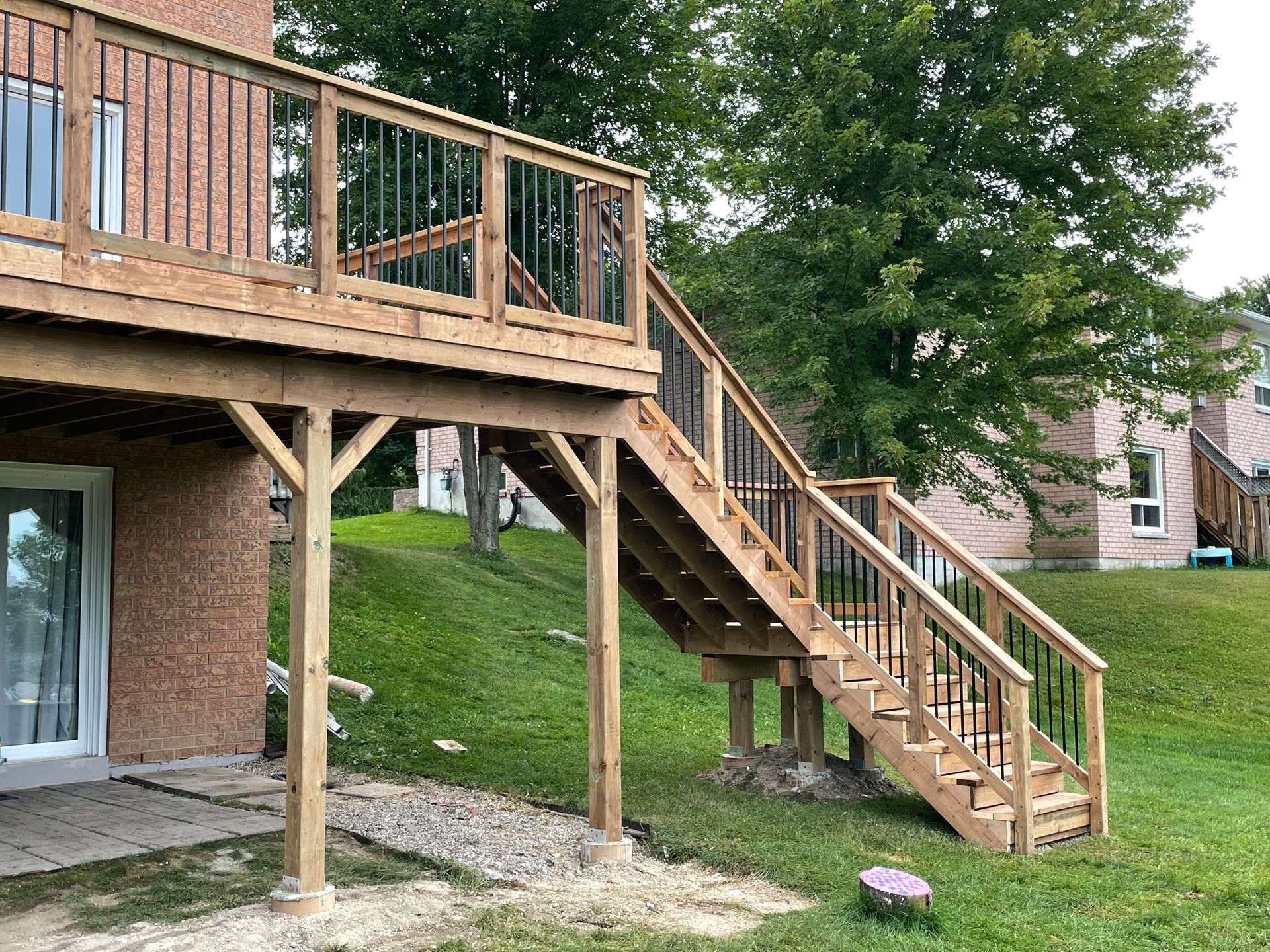 A wooden deck with stairs leading up to it is in the backyard of a house.