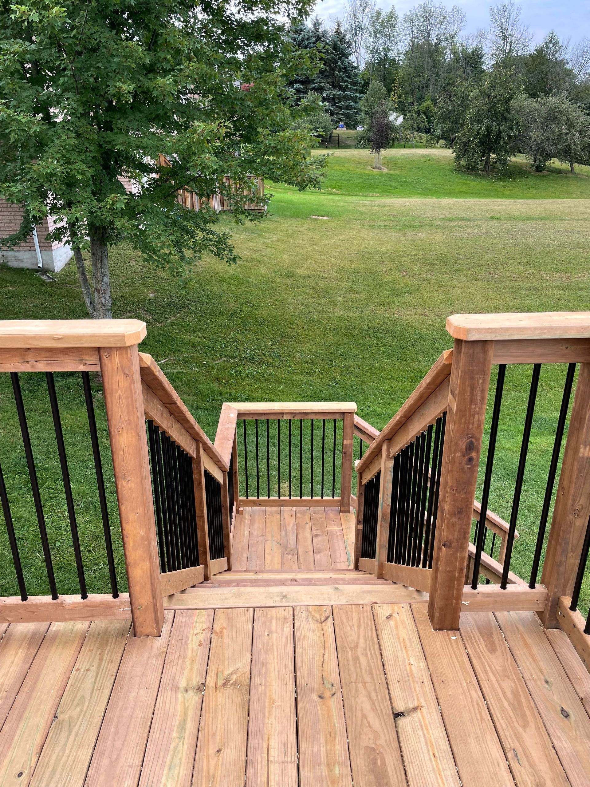 A wooden deck with stairs leading up to a grassy field.