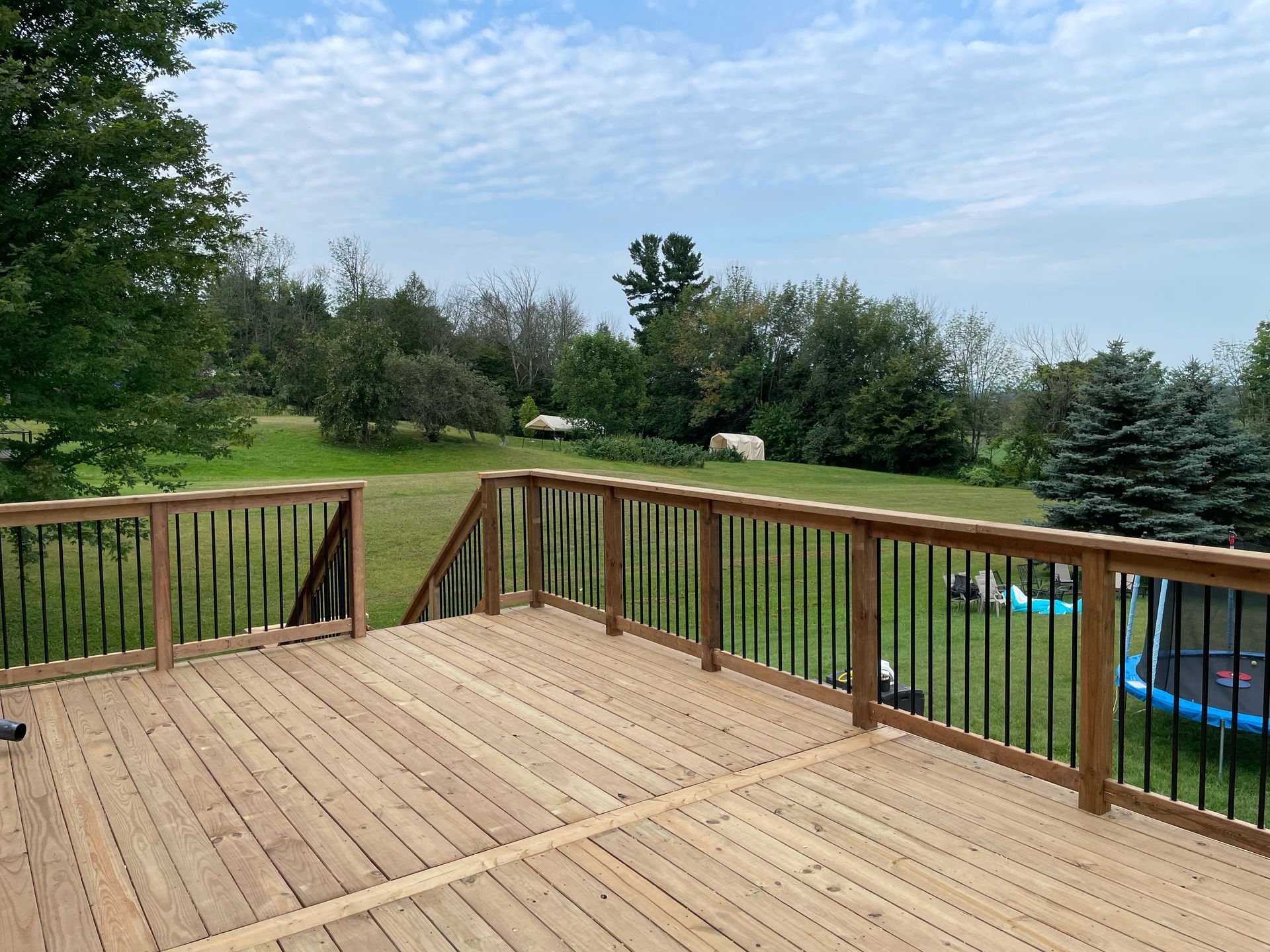 A wooden deck with a metal railing overlooking a lush green field.