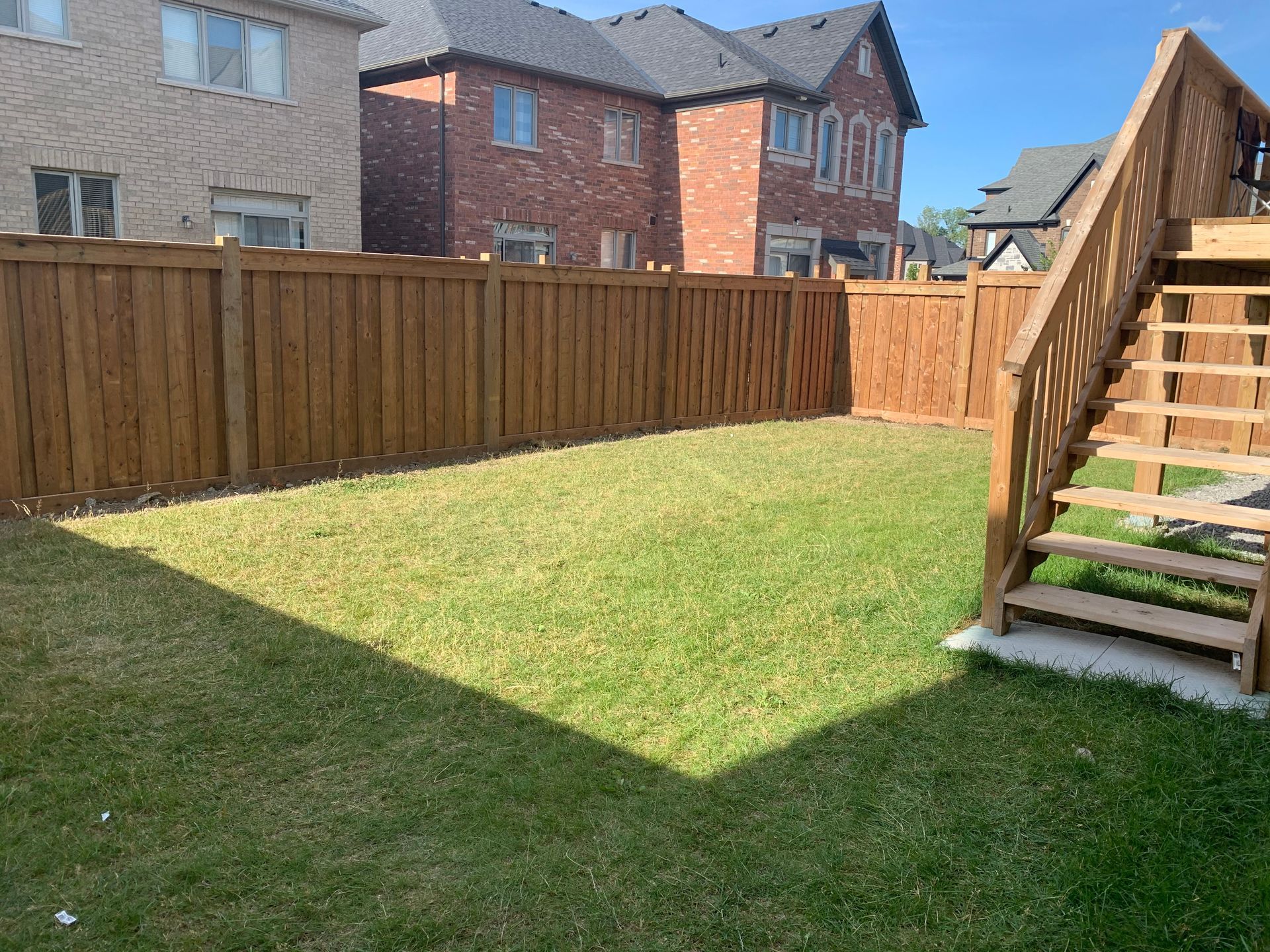 A backyard with a wooden fence and stairs leading to a deck.
