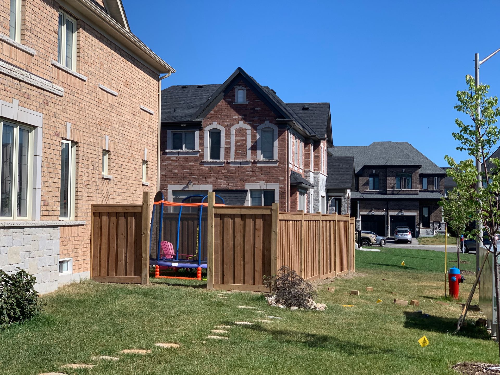 A backyard with a wooden fence and a playground in front of a brick house.