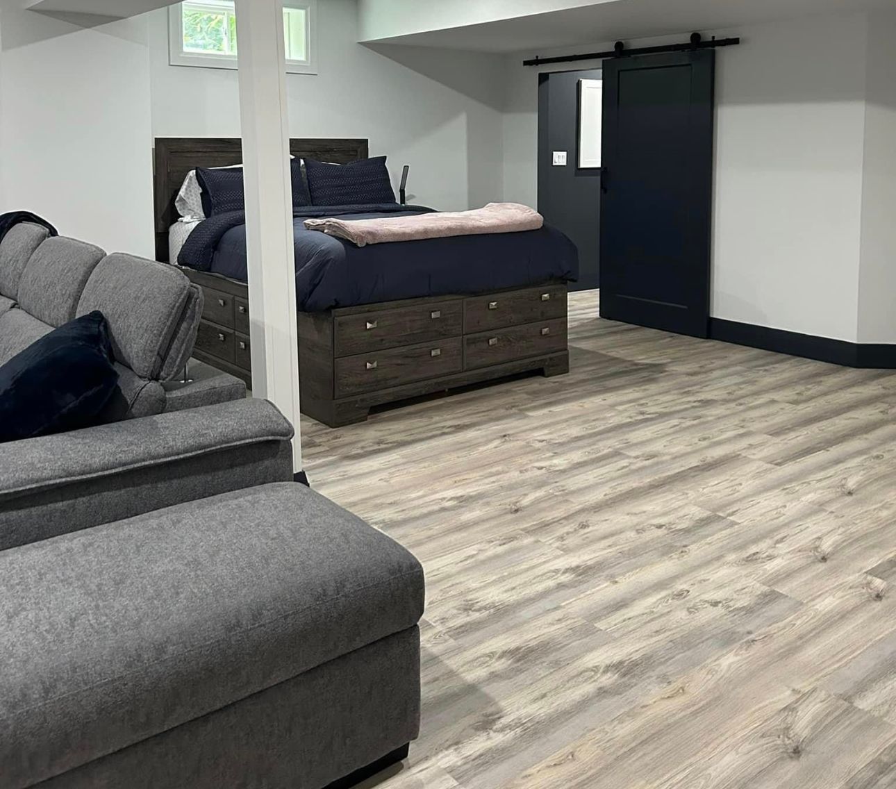 A living room with a couch , bed , dresser and sliding barn door.