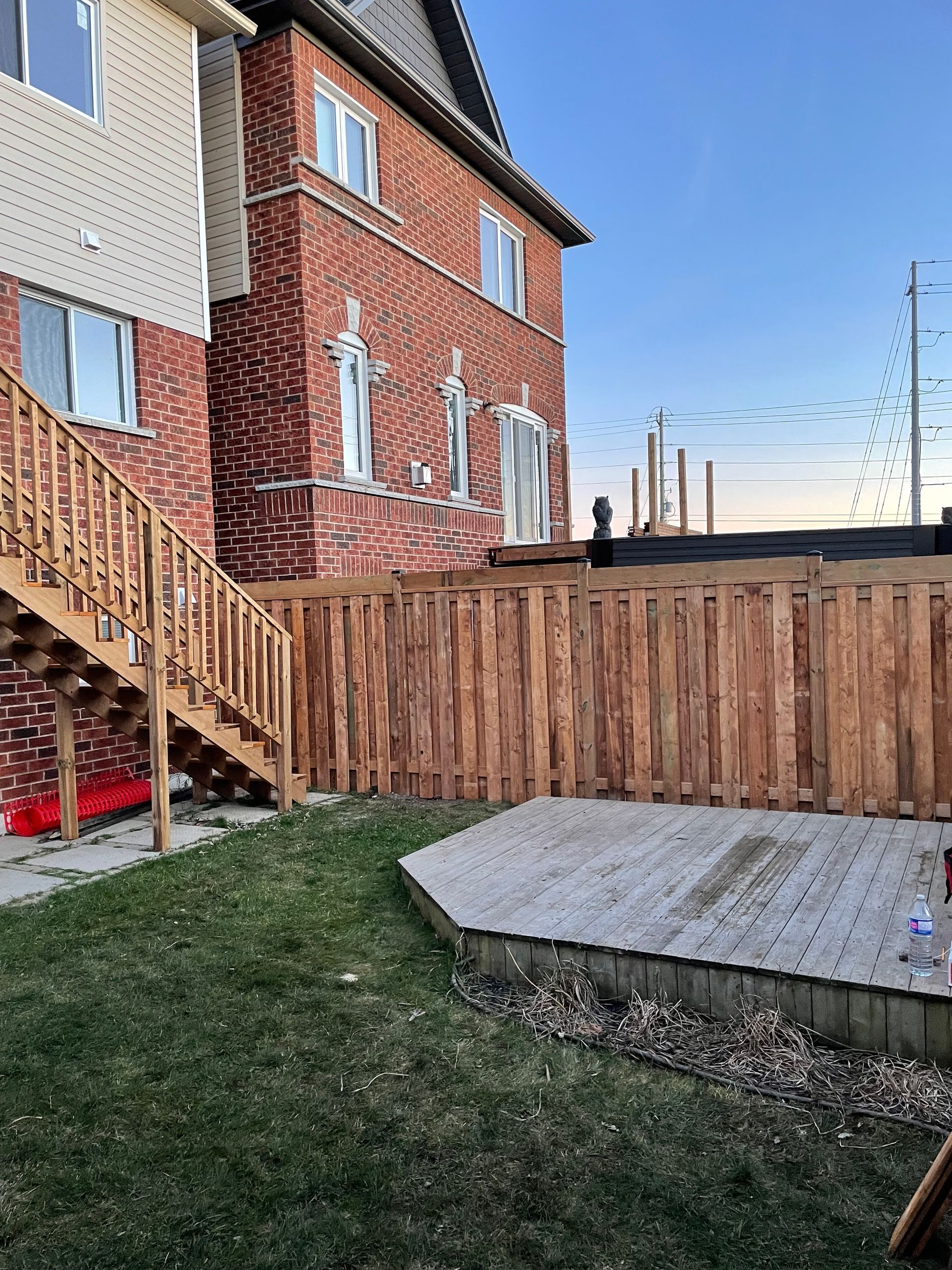 A brick house with a wooden fence and stairs in the backyard.