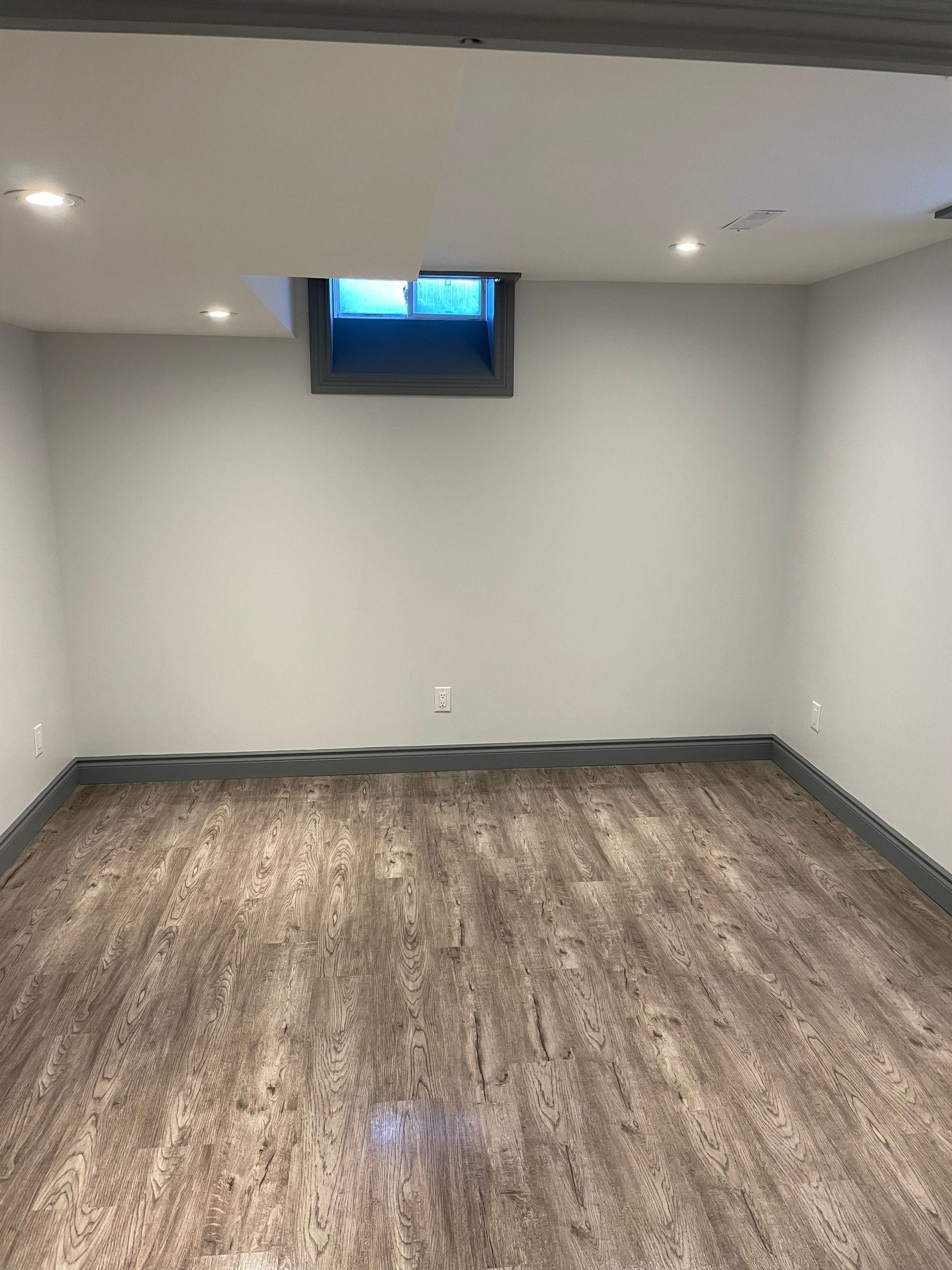 An empty basement with hardwood floors and a window in the ceiling.
