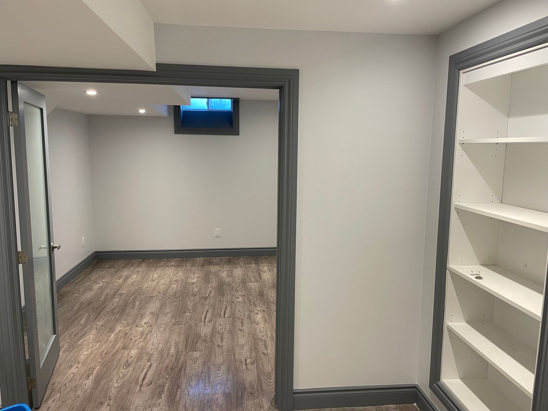 An empty basement with hardwood floors and shelves.