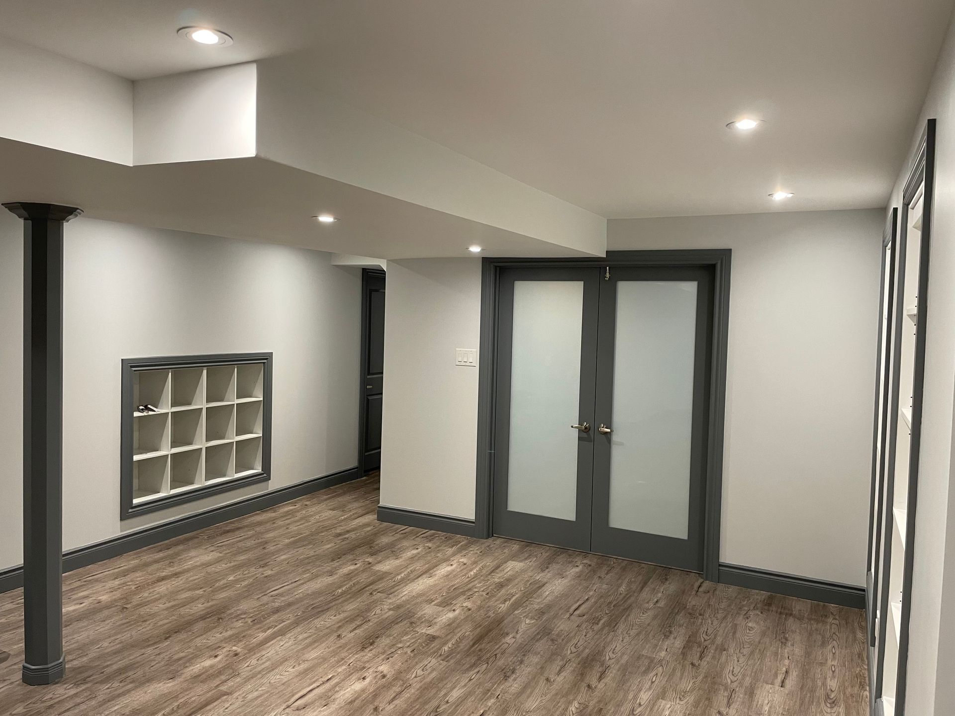 An empty basement with hardwood floors and white walls.
