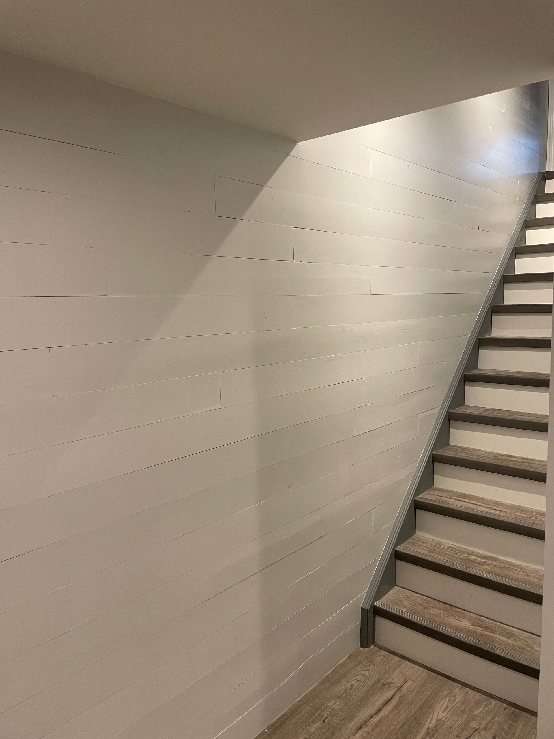 A staircase in a basement with a white wall and wooden steps.
