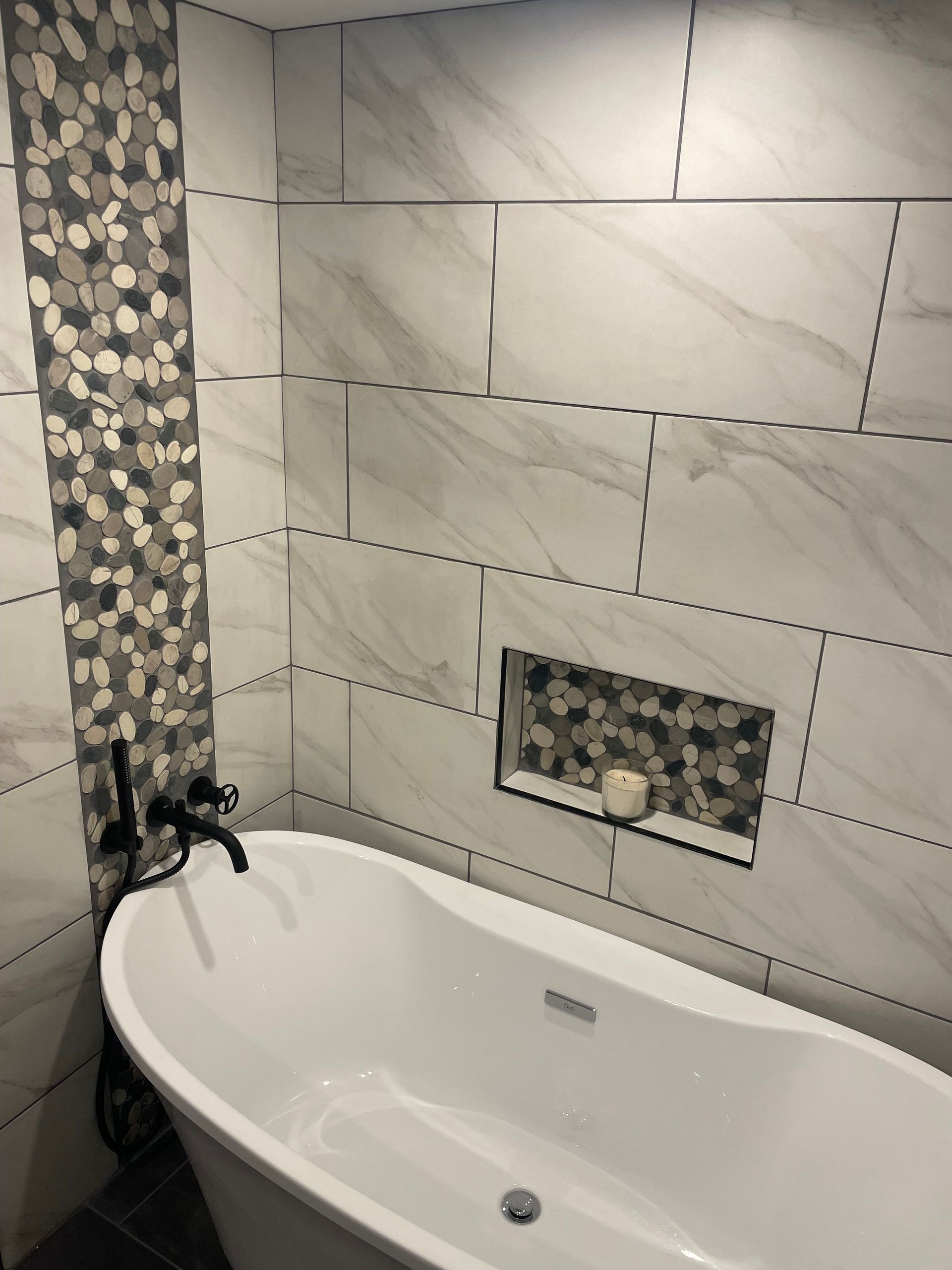 A bathtub in a bathroom with marble tiles on the wall