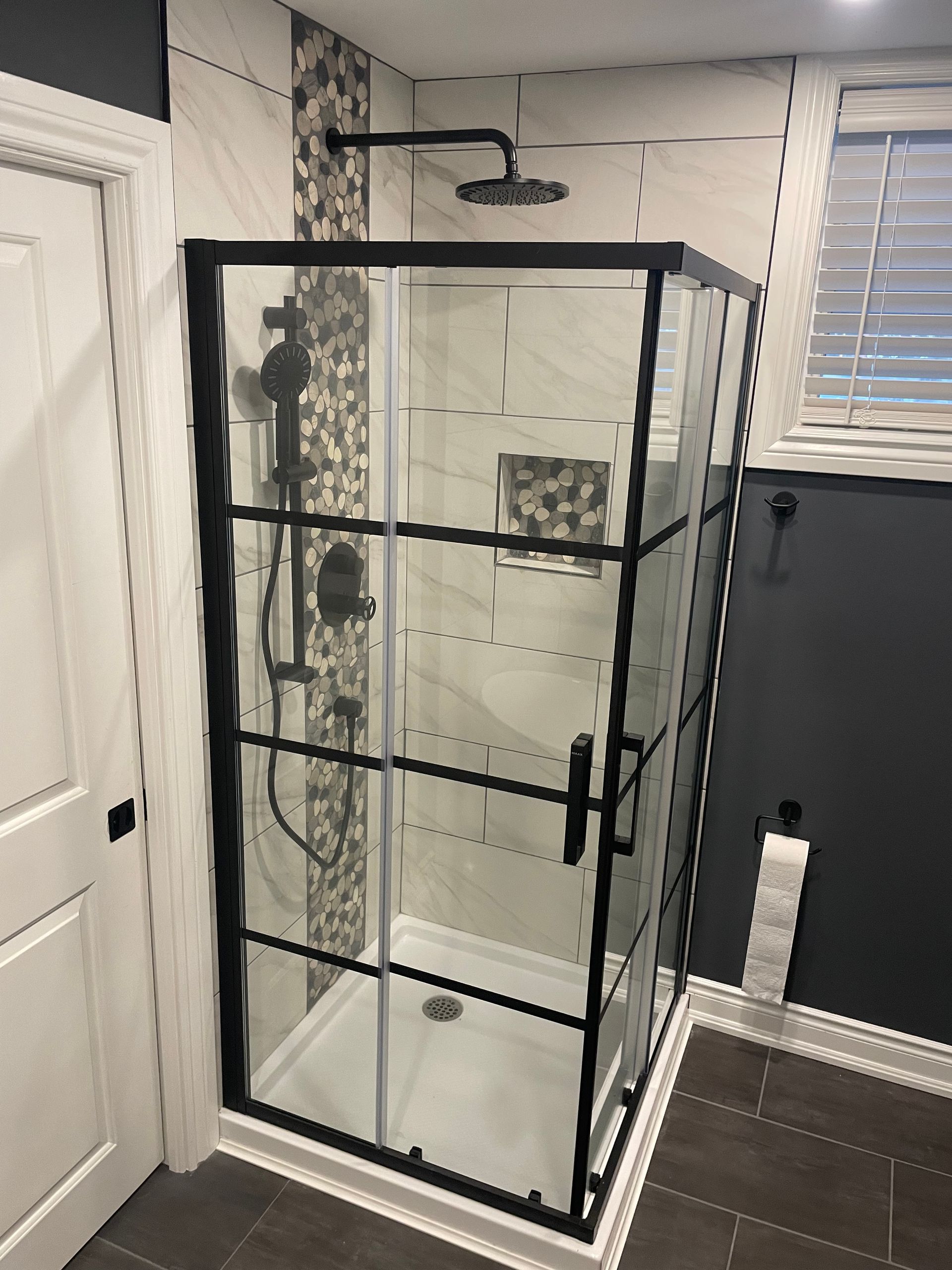 A bathroom with a shower stall with a black frame and a shower head.