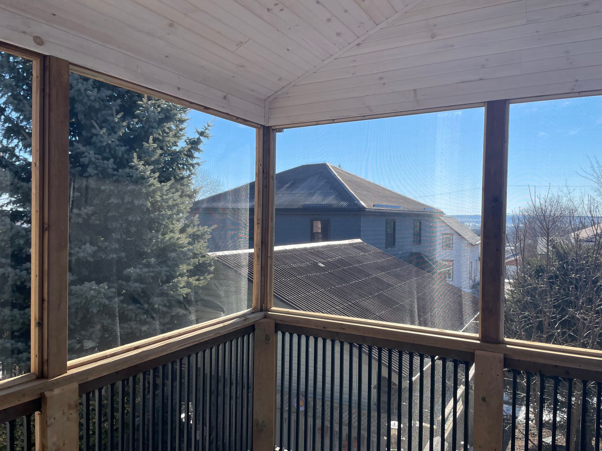 A screened in porch with a view of a house and trees.