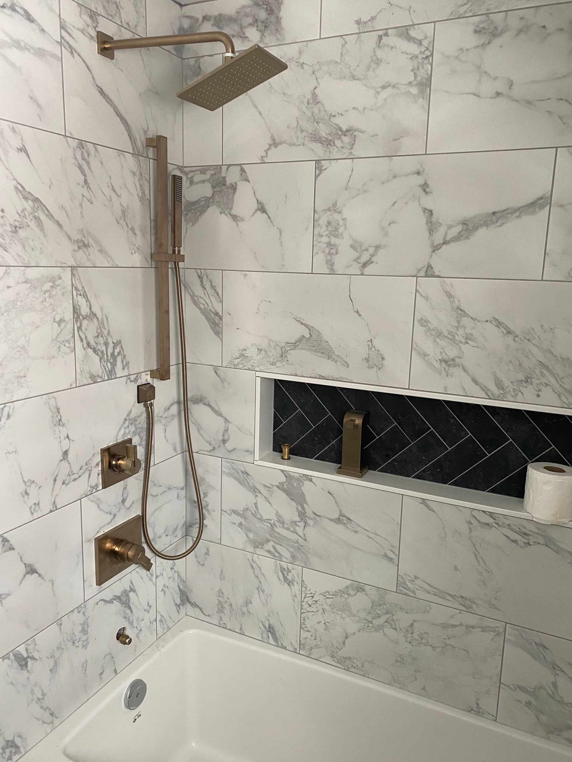 A bathroom with marble tiles , a tub and a shower head.
