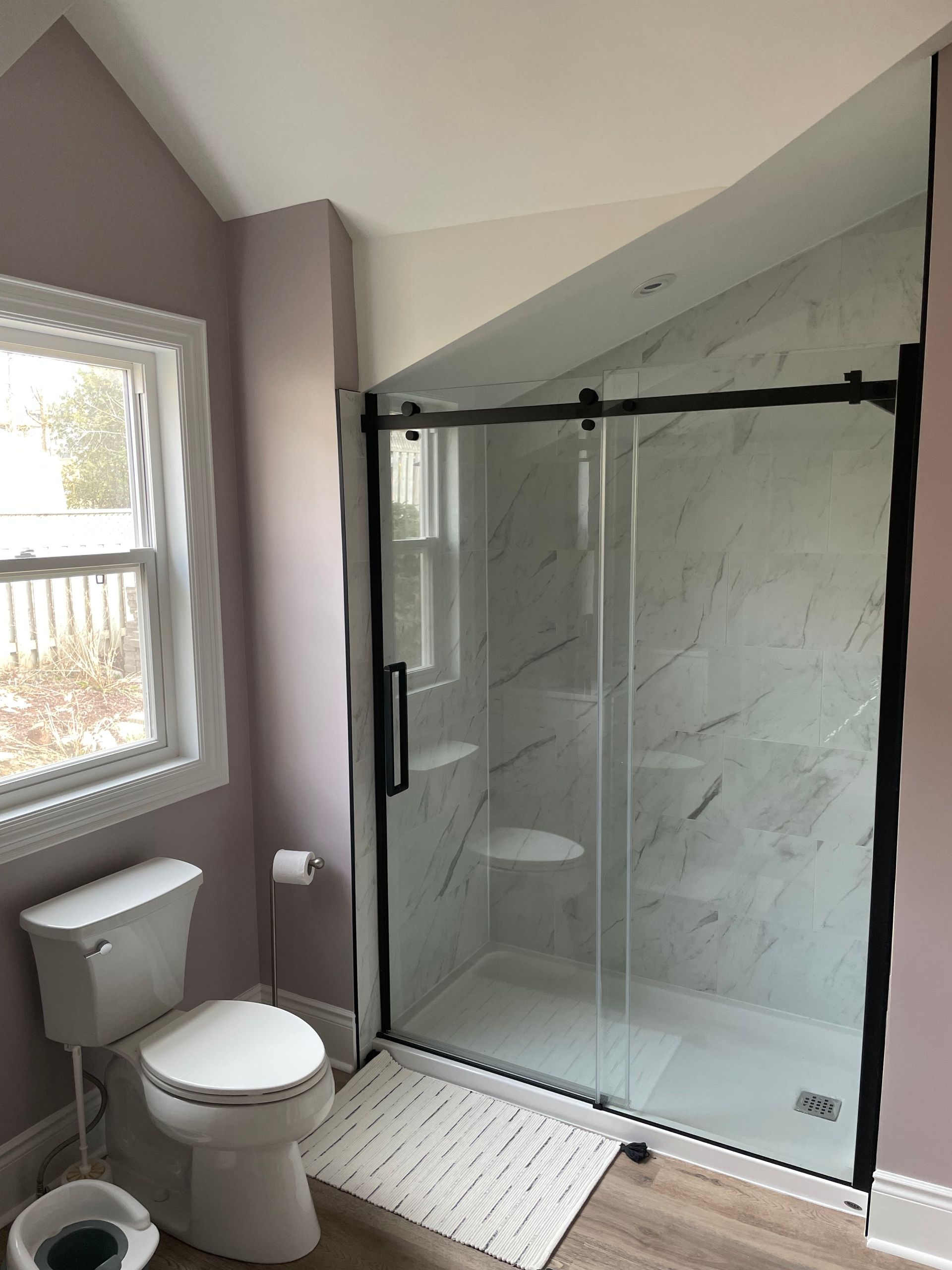 A bathroom with a toilet , shower , and window.