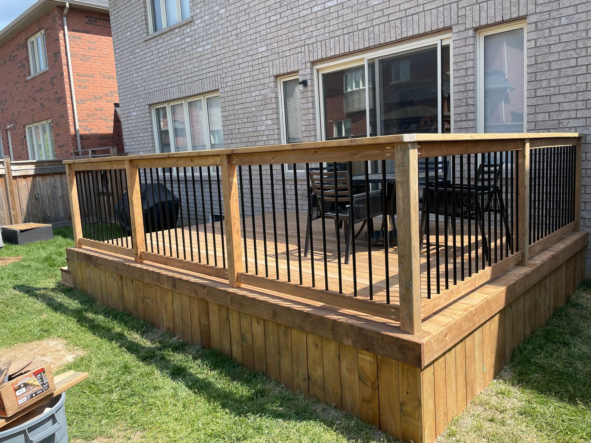 A wooden deck with a metal railing in front of a brick house.