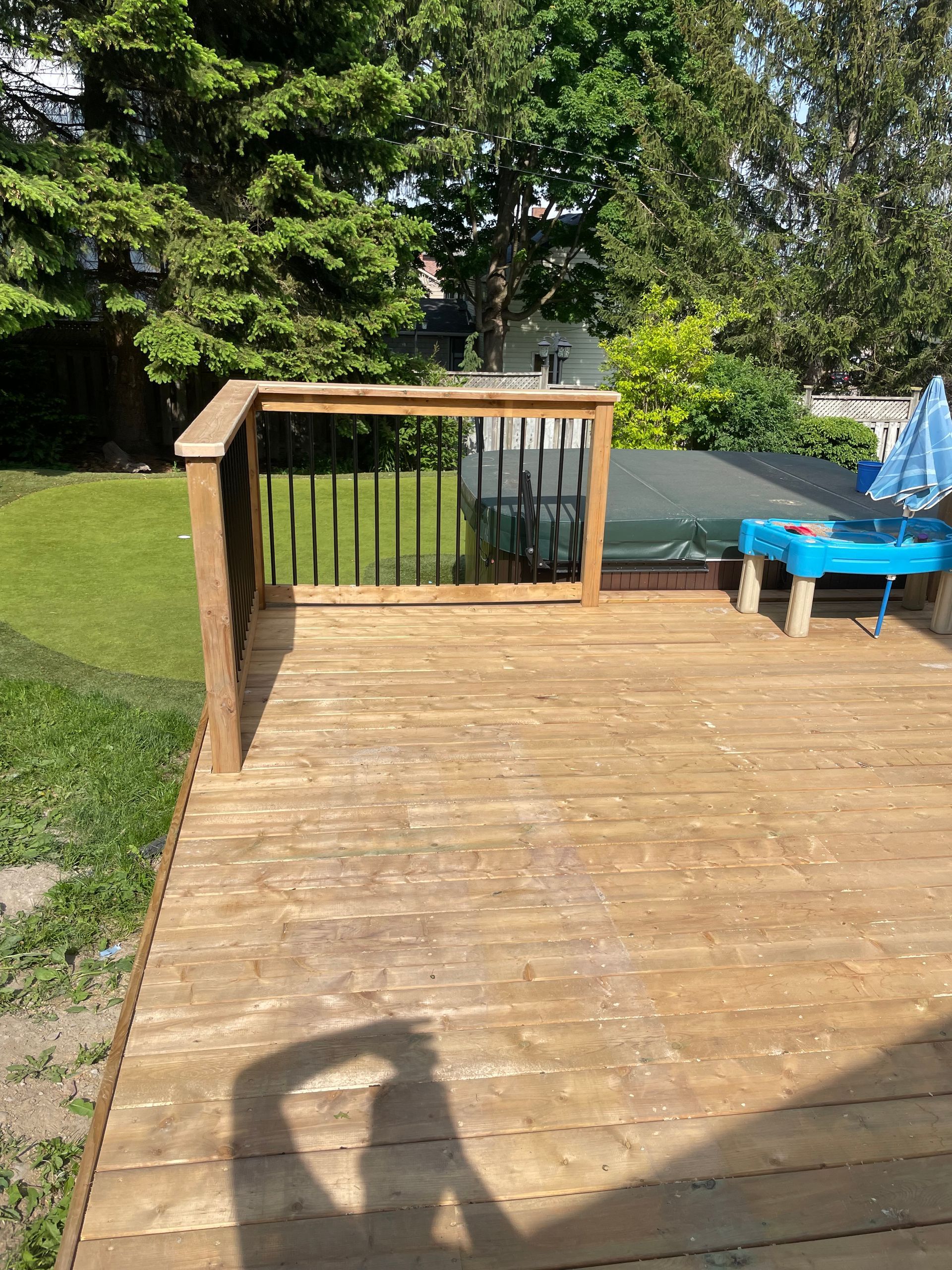A wooden deck with a blue table and umbrellas in the backyard.
