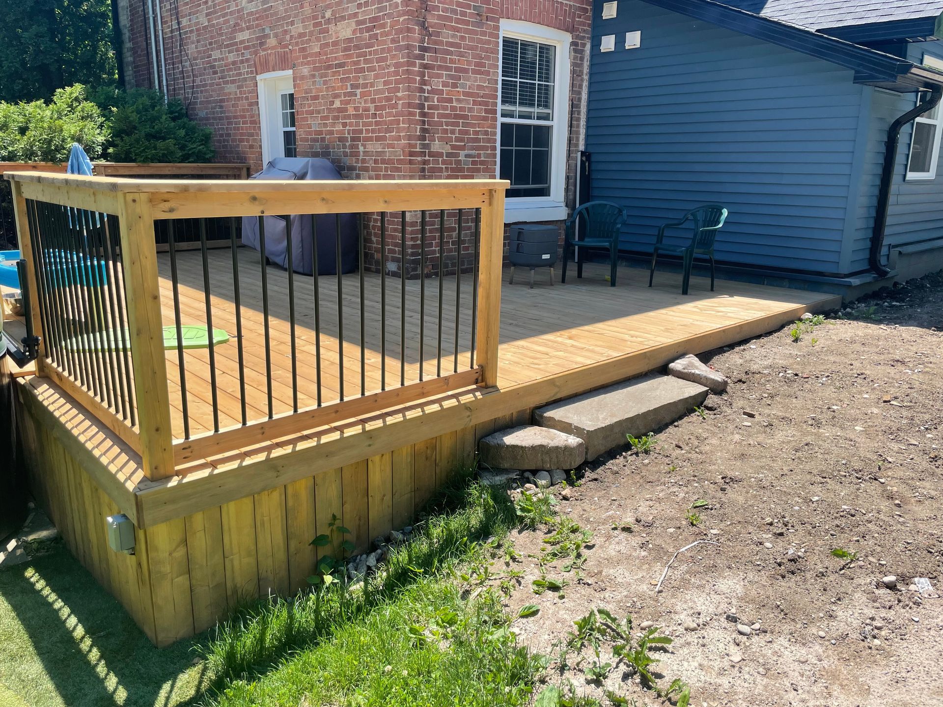 A wooden deck with a metal railing in front of a blue house.