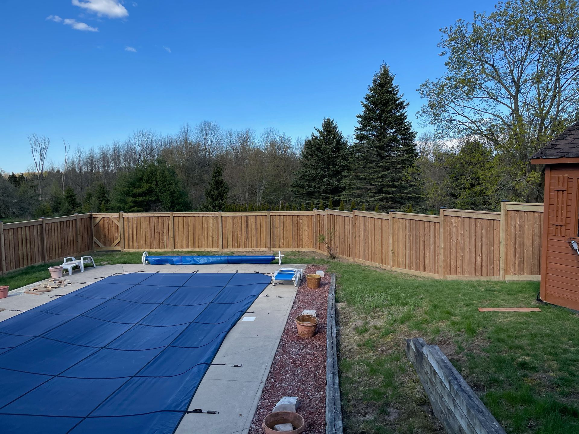 A wooden fence surrounds a swimming pool with a blue cover.