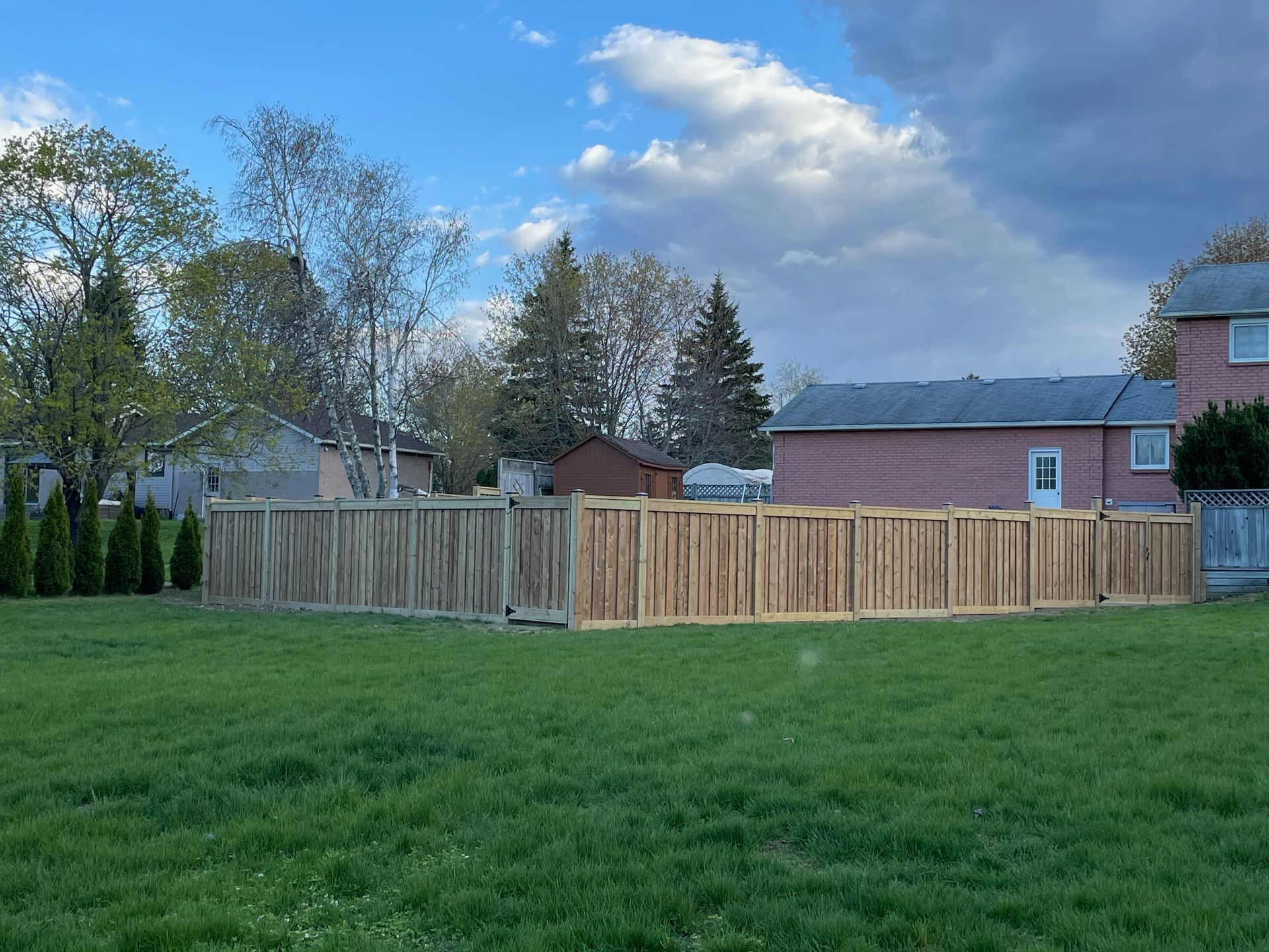 A wooden fence surrounds a lush green field in front of a brick house.