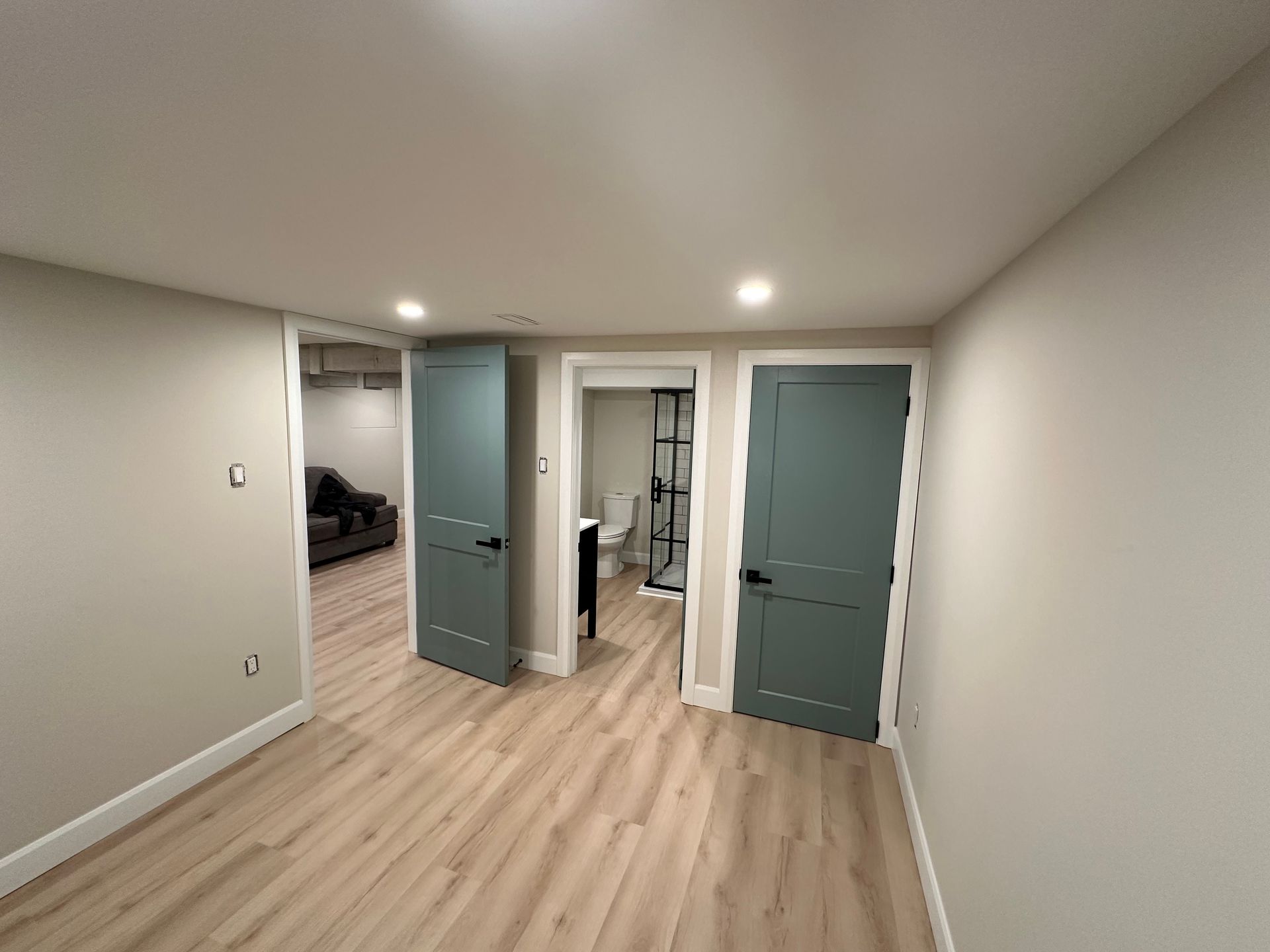 A basement with hardwood floors and blue doors leading to a bathroom and a living room.