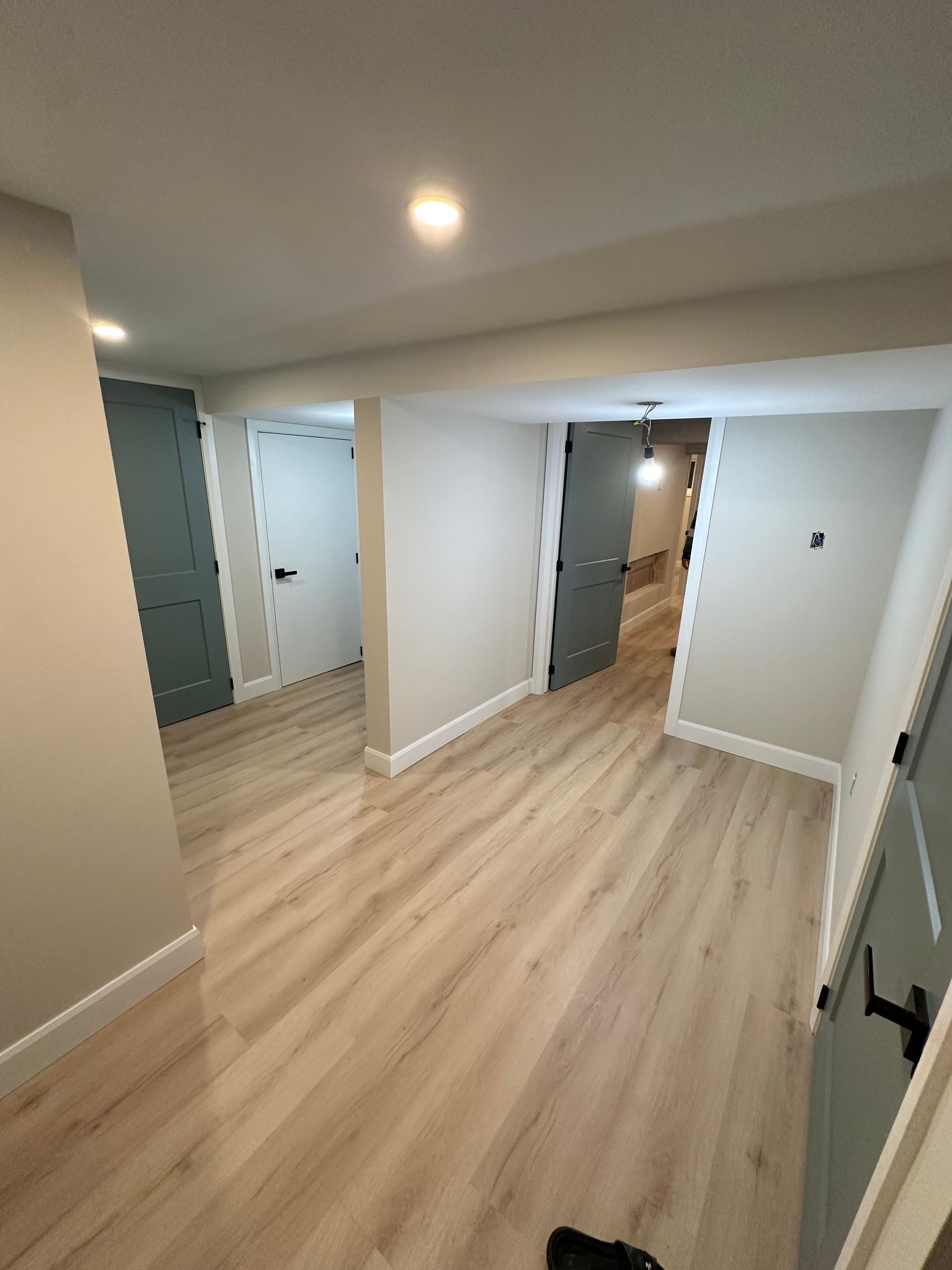 A hallway in a basement with hardwood floors and white walls.