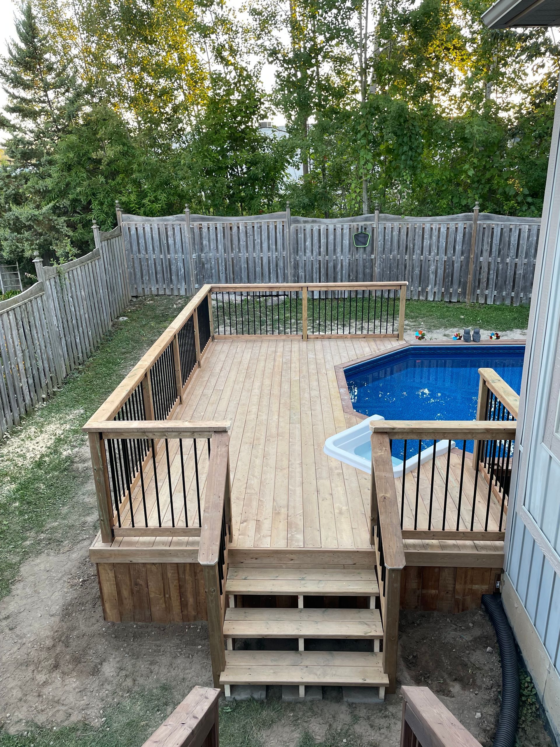 A wooden deck next to a swimming pool in a backyard.