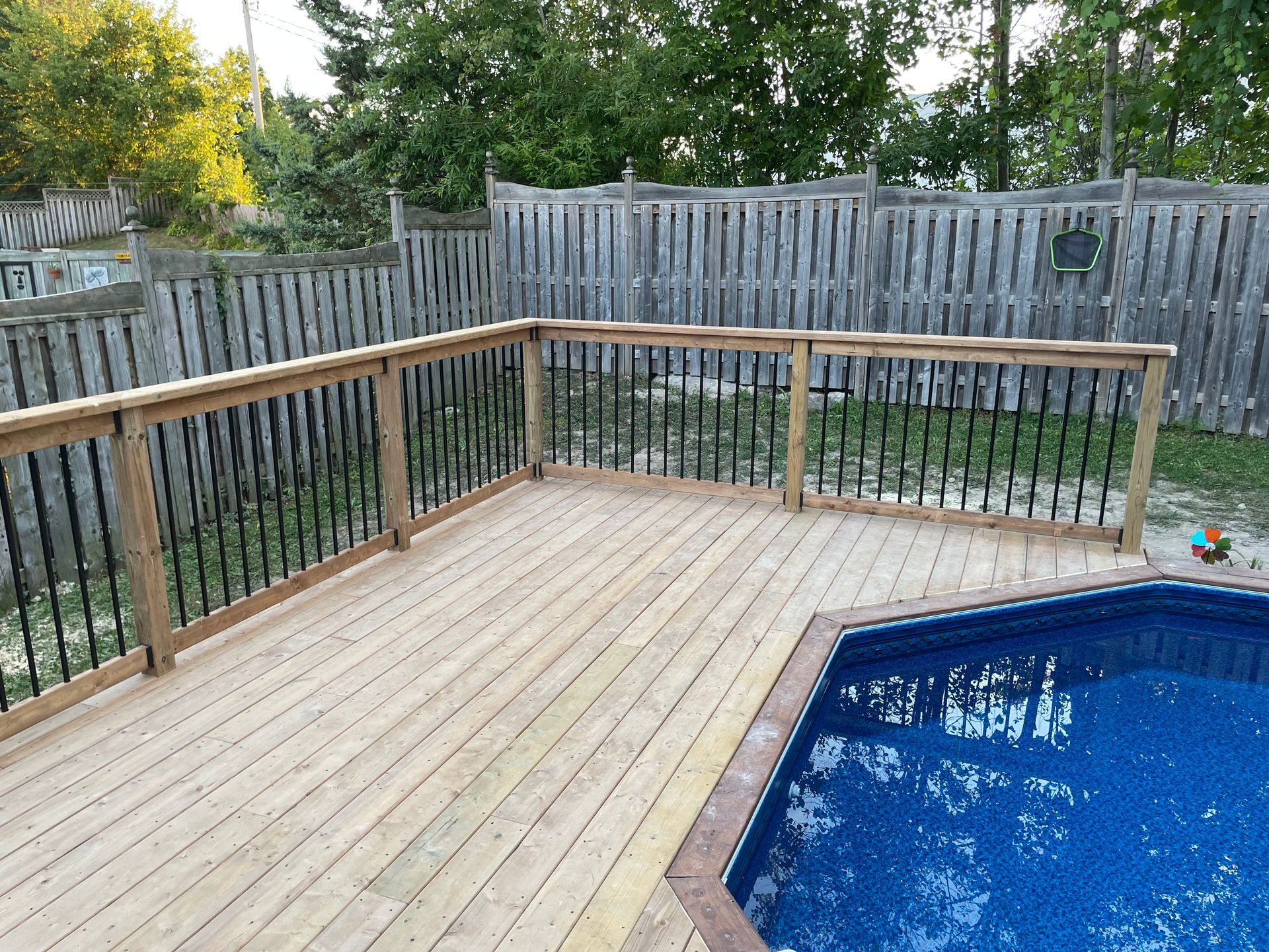 A wooden deck overlooking a swimming pool with a fence in the background.
