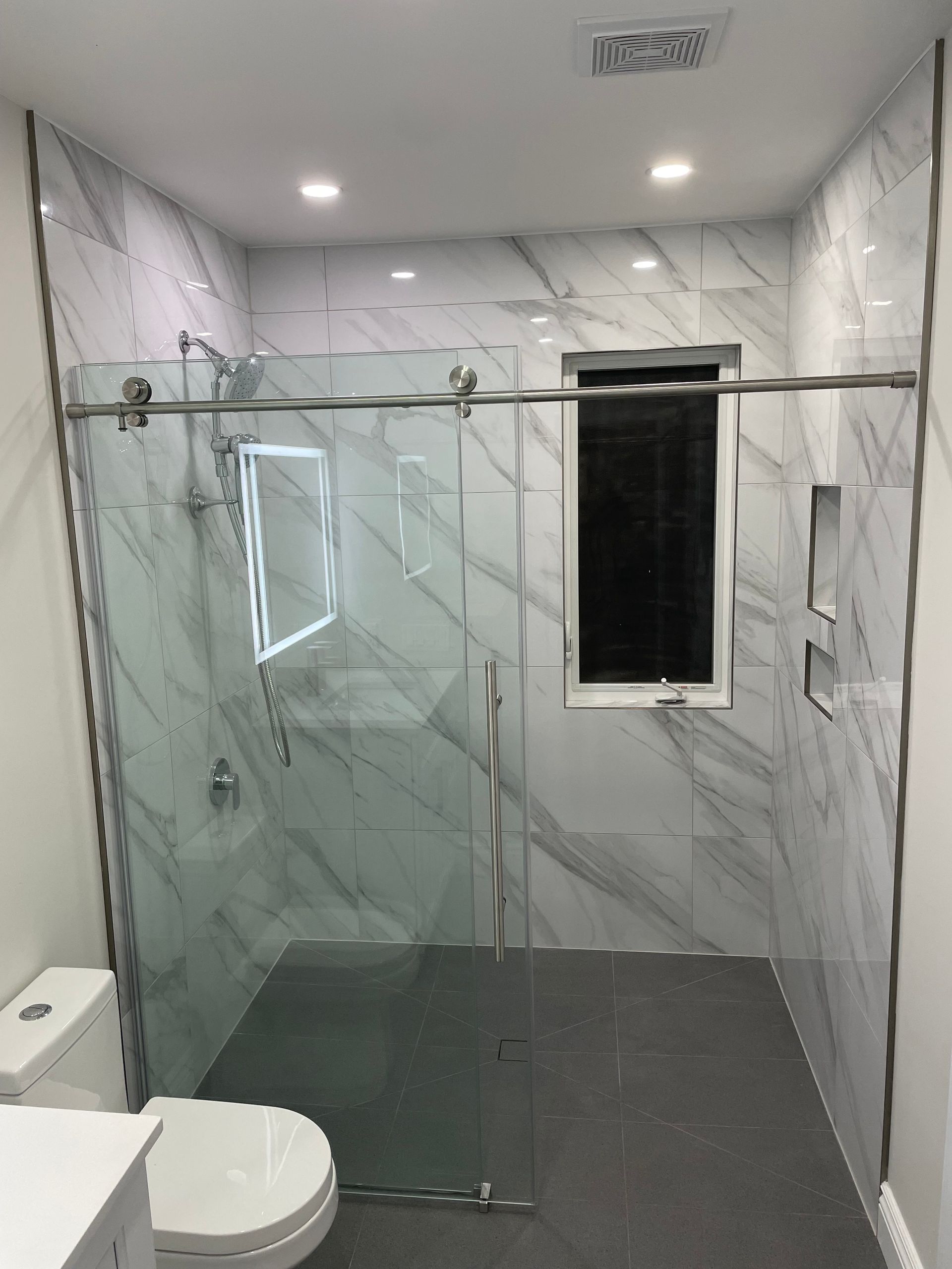 A bathroom with a toilet , shower and window.