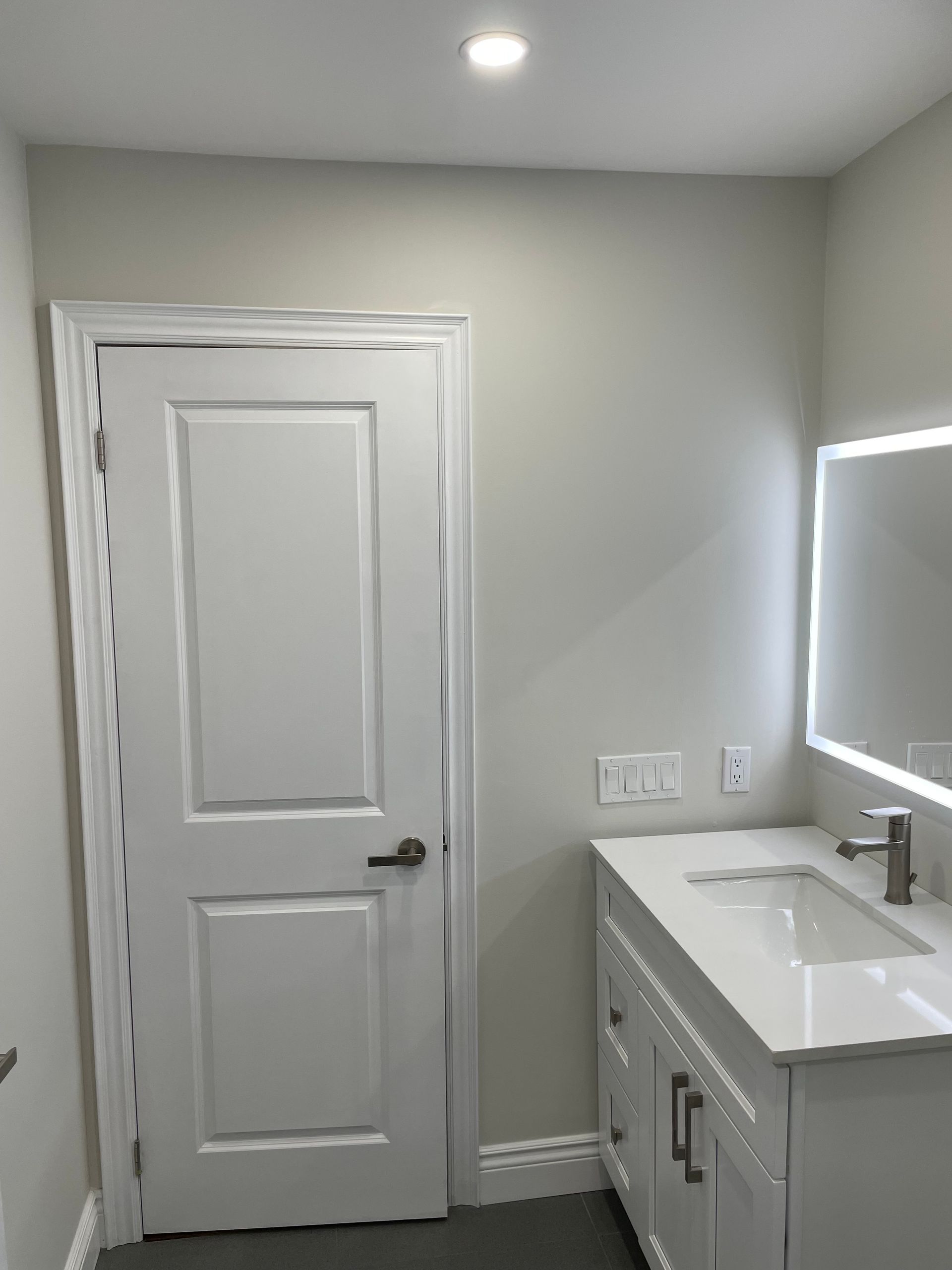 A bathroom with a sink , mirror and door.