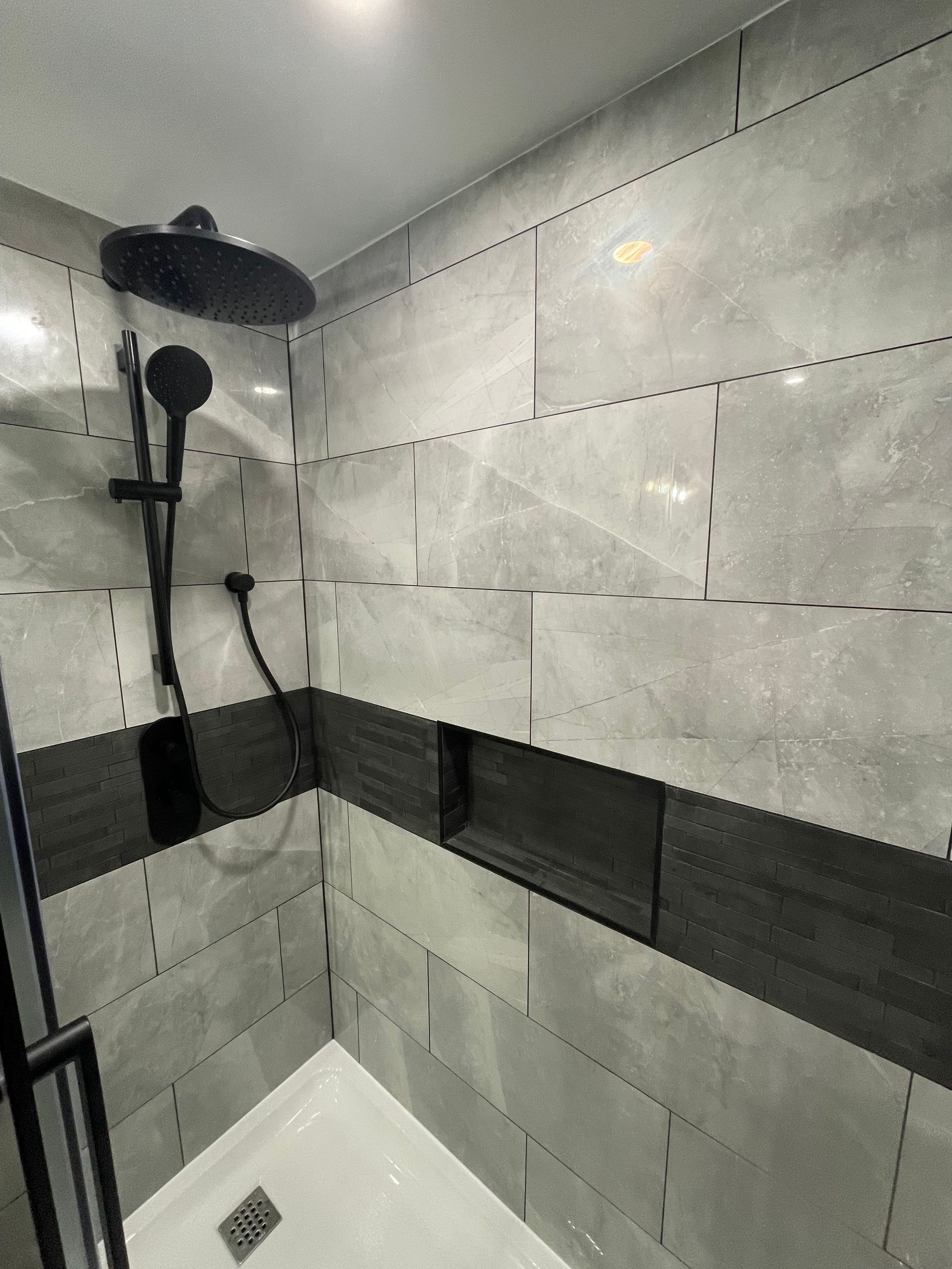 A shower with a black shower head and black and white tiles.
