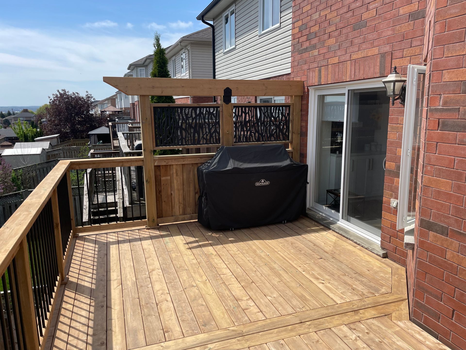 A wooden deck with a grill on it next to a brick building.