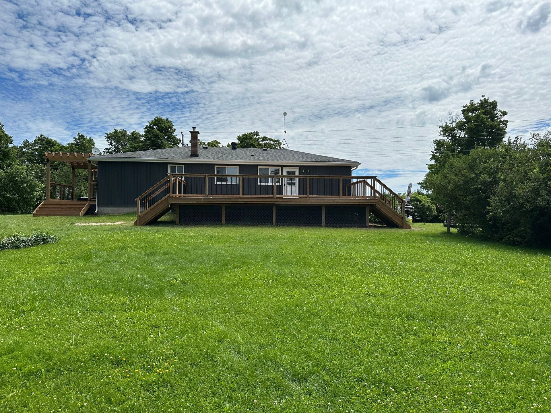 A house with a large deck is sitting on top of a lush green field.