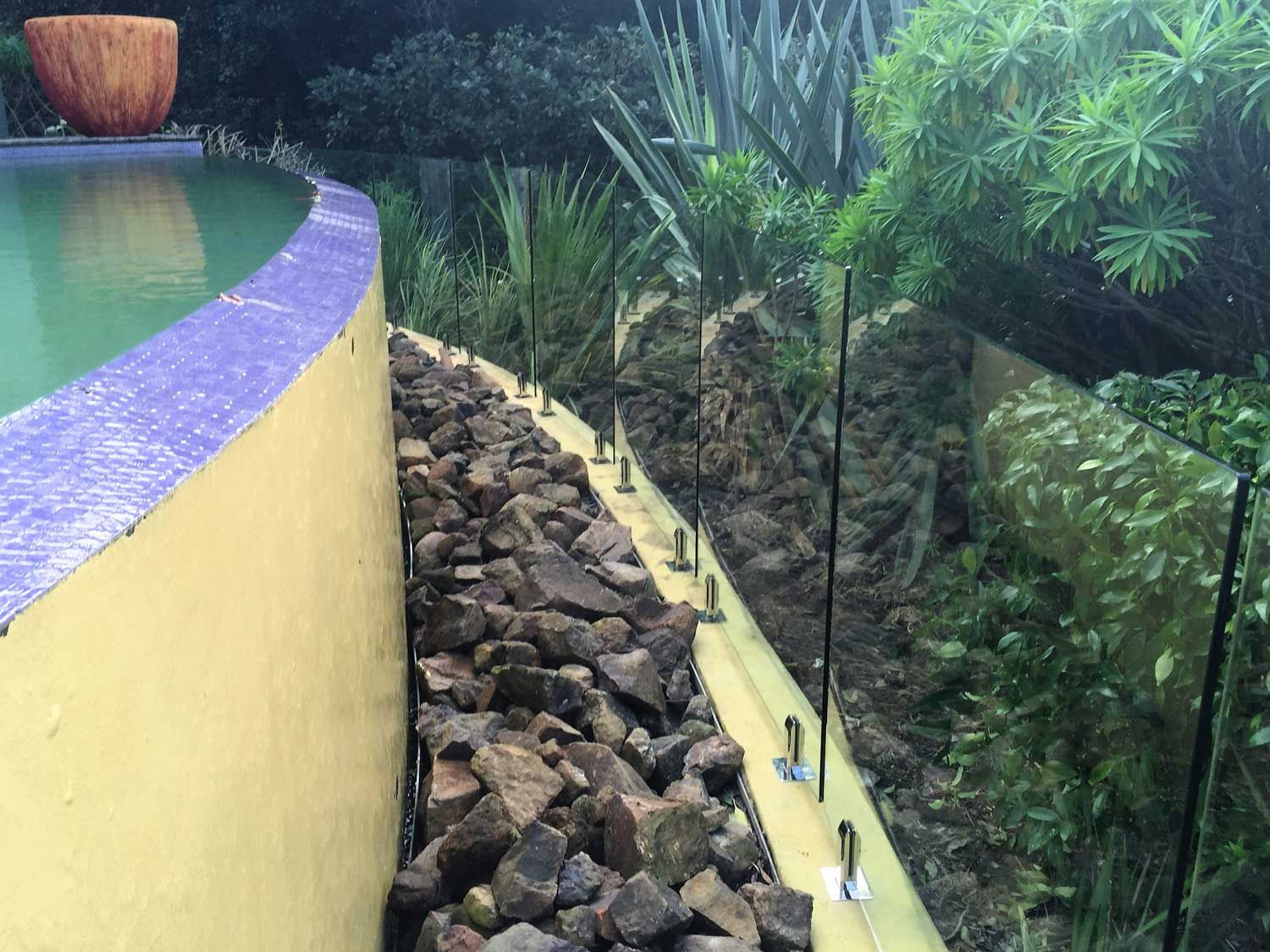 A Pool Yellow Paint Wall and Glass Fencing — Glass Windows & Doors in Shoalhaven, NSW