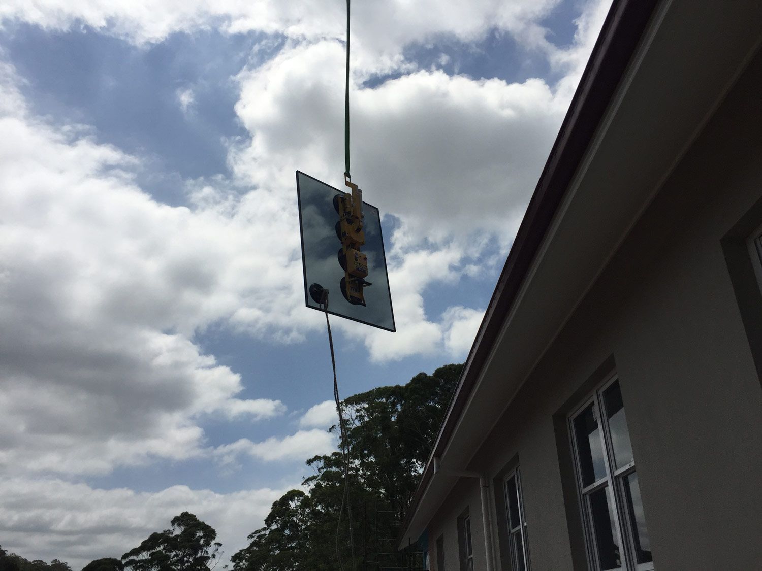 A Crane is Holding Small Piece of Glass Towards the Window Frame — Glass Windows & Doors in Shoalhaven, NSW