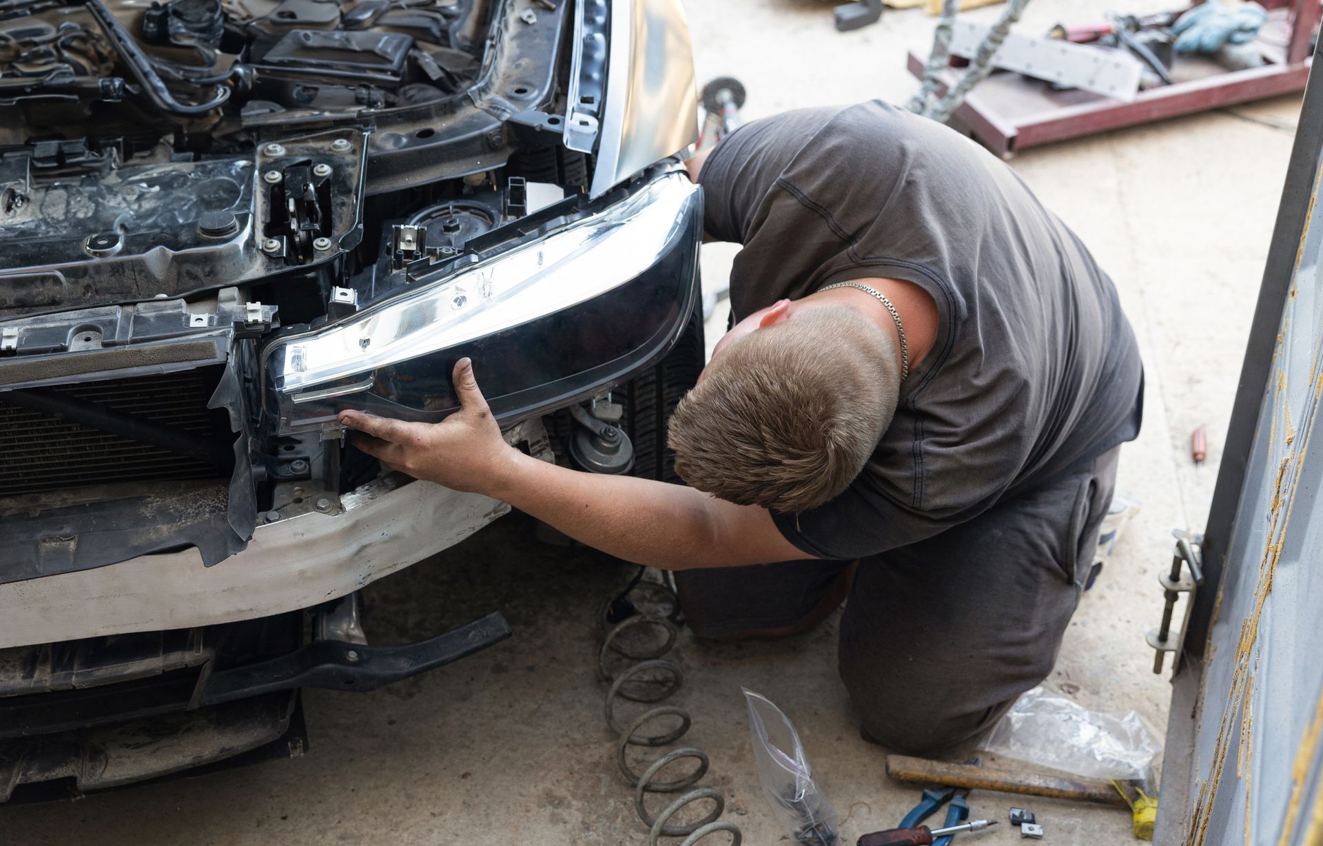 A man is working on the front of a car in a garage.