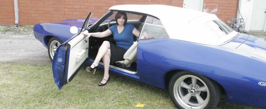 A woman is sitting in a blue car with her legs crossed