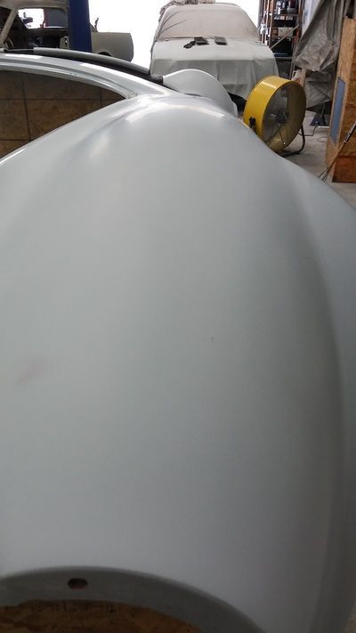 A white car hood is sitting in a garage next to a yellow fan