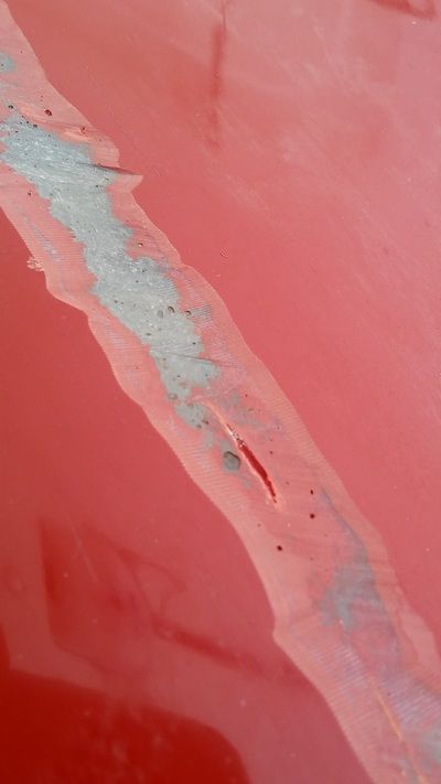 A close up of a red car with a scratch on the hood