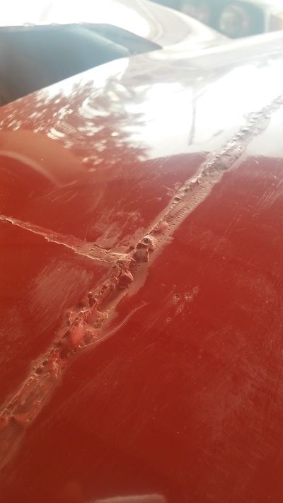 A close up of a red car hood with a scratch on it