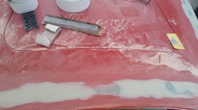 A red car hood is being repaired with sandpaper and tape