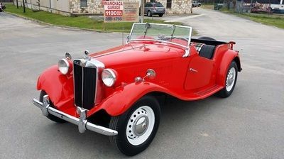 A red vintage car is parked in a parking lot in front of a building