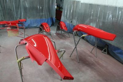 A bunch of red fenders are sitting on a table in a paint booth