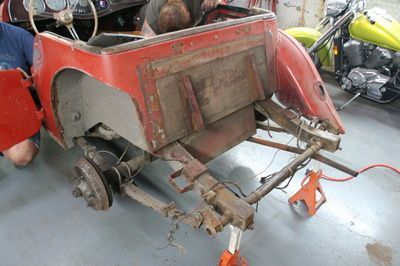 A man is working on a red car in a garage next to a motorcycle