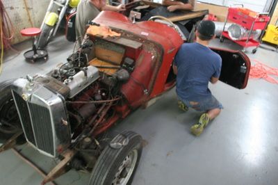 Two men are working on an old red car in a garage